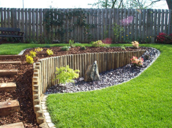 A loping garden contoured using timber posts to create a more useable lawn area