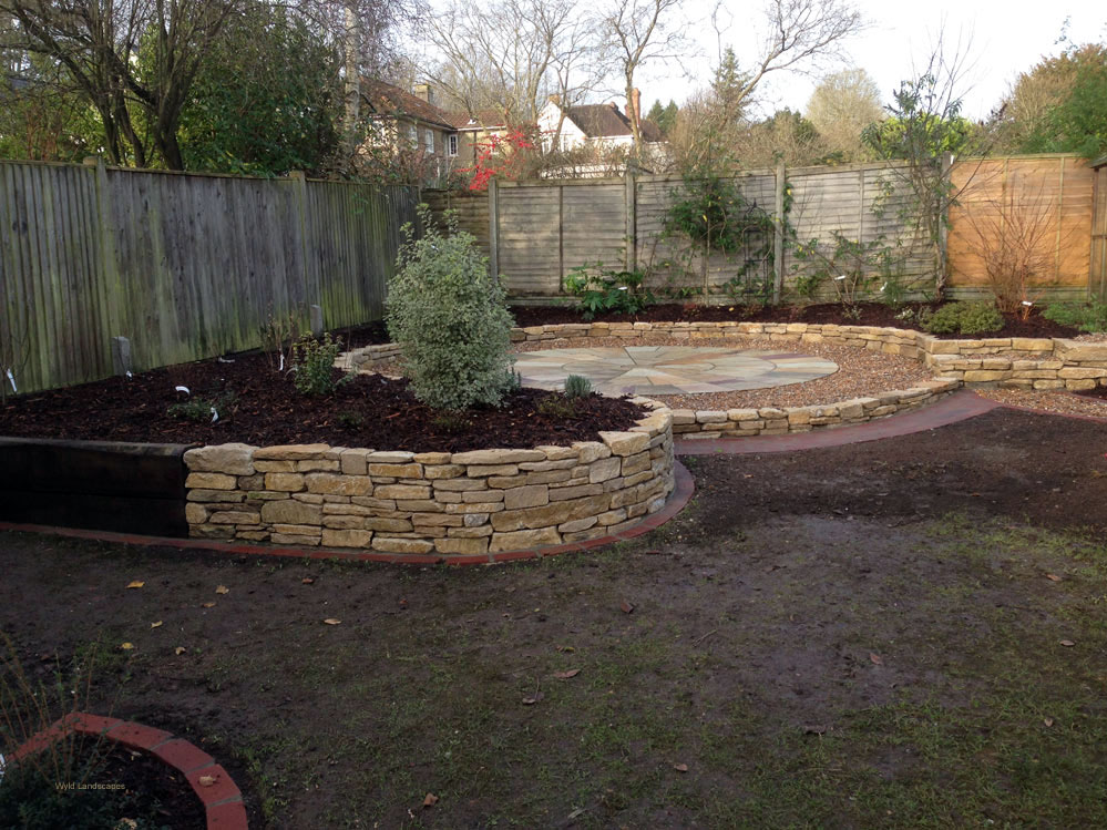 An area of an existing garden re-developed to include a paved circle using Indian sandstone slabs, a purbeck stone raised bed, a brick path and brick edges to the lawn and planted borders mulched with bark and weed supressing sheet to keep maintenance to a minimum
