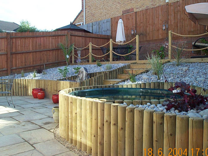 A sloping garden terraced with timber poles with a lower patio and an upper deck area with rope balustrade.
