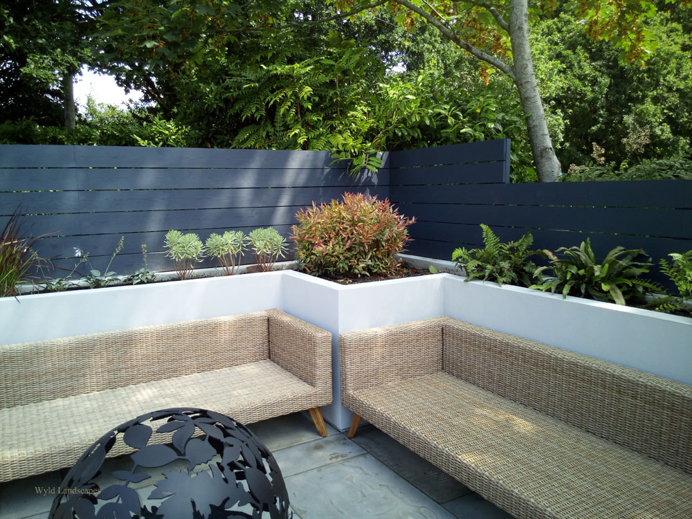 Part of a seating area surrounded with raised beds and screening from a parking area