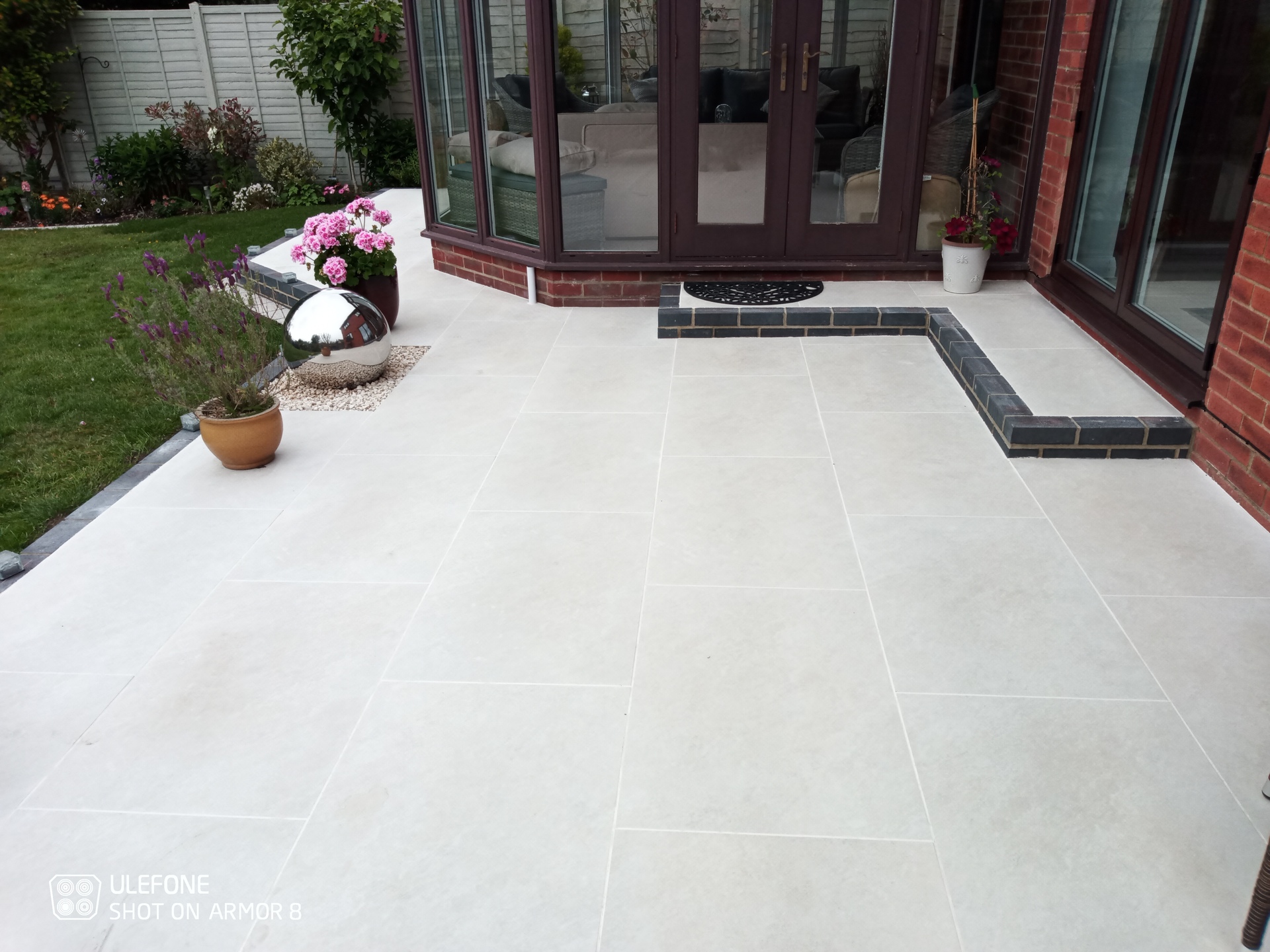 A large porcelain patio with steps, retaining wall, brick edging, paved path and covered seating area